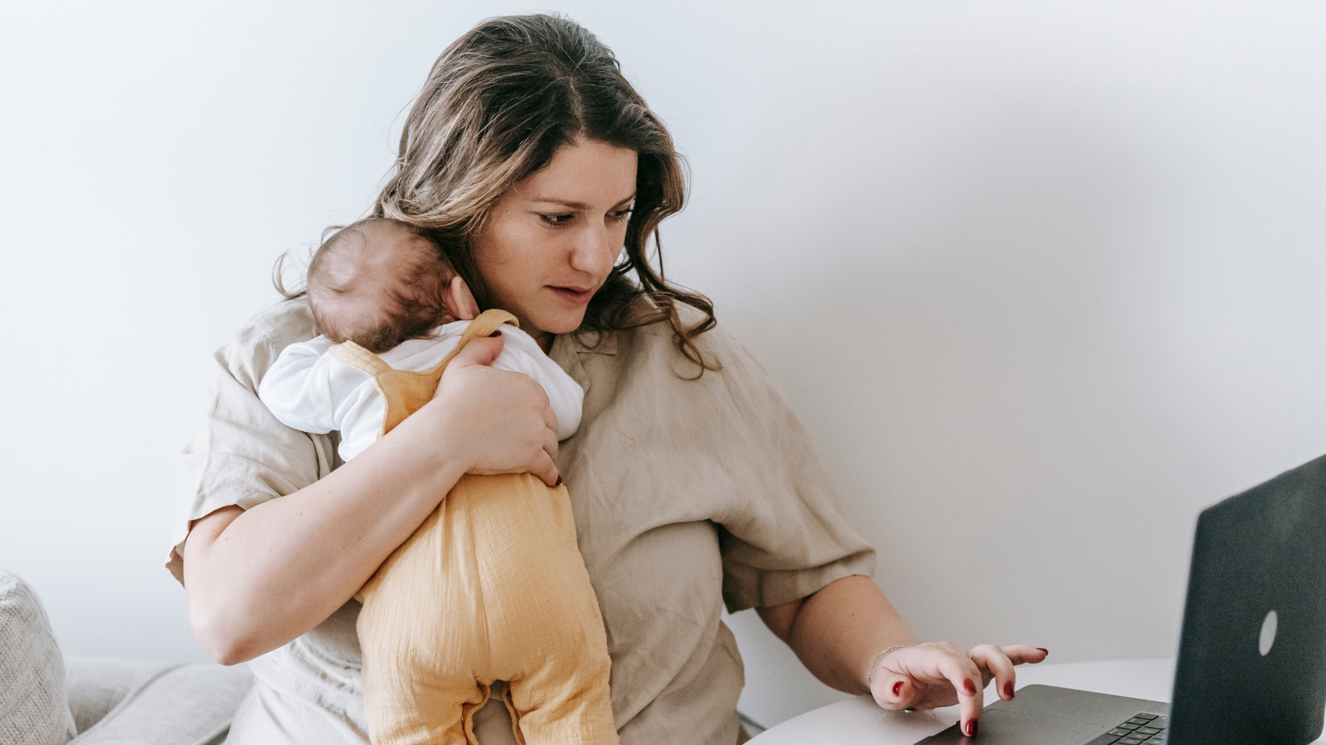 A lady holding her baby whilst using a laptop